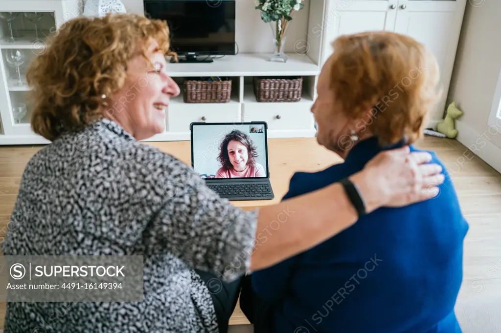 Back view of cheerful senior women chatting with friend during online video meeting via laptop while staying at home during coronavirus lockdown