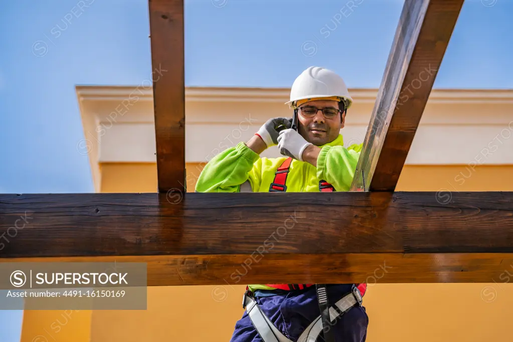 From below of male technician in work wear standing on scaffolding and preparing for installation of solar panel on wooden construction