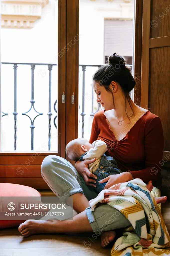 Happy mother breastfeeding baby near window