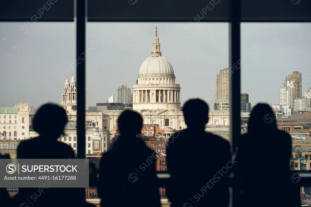 Back view silhouettes of travelers standing near window at viewpoint and admiring view of Saint Paul Cathedral in London