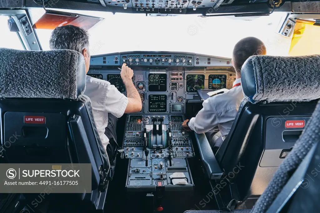 Back view of male pilot and co pilot using instrument panel in cockpit of modern passenger aircraft during flight