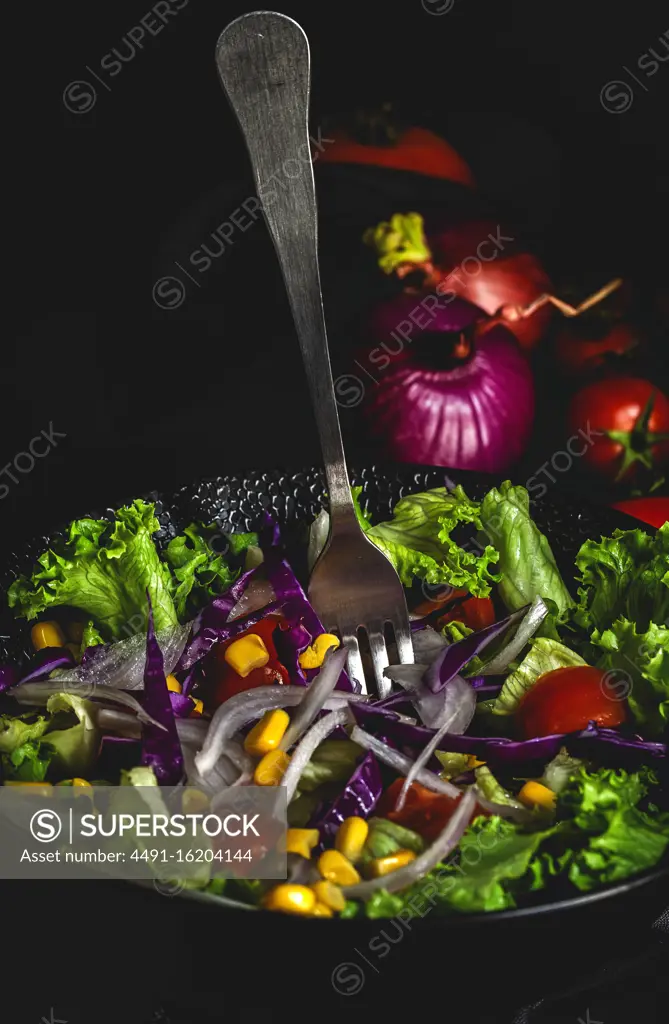 Healthy vegan food with fresh lettuce, cherries tomatoes, red onion and corn on dark background