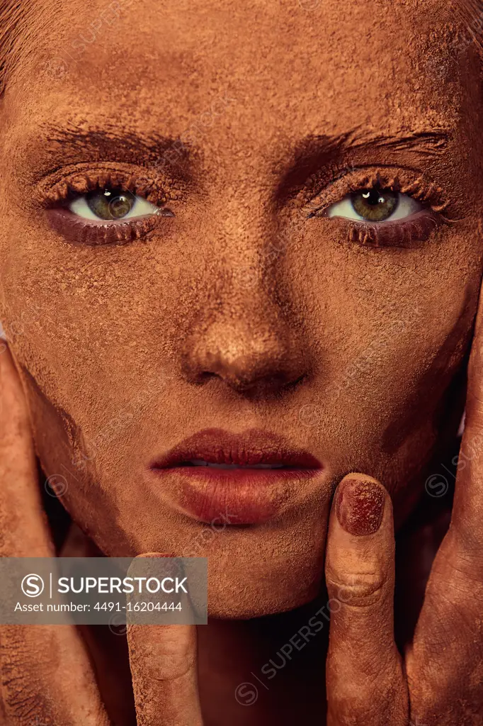 Young beautiful woman with chocolate powder on face touching skin and looking at camera