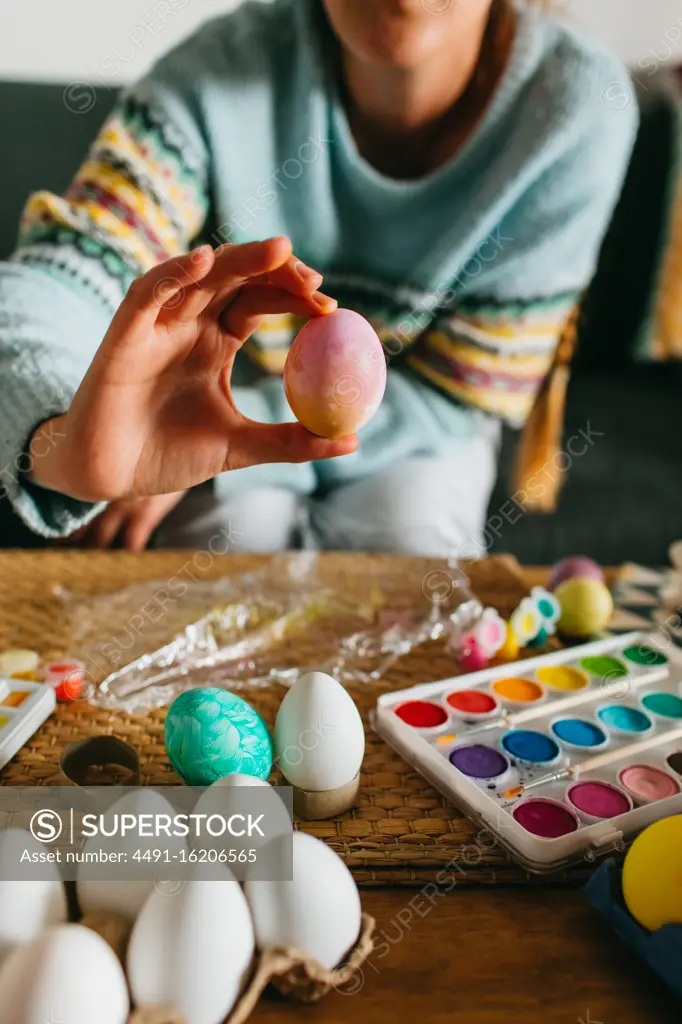 Cropped anonymous person demonstrating finished Easter egg over table with watercolor at home