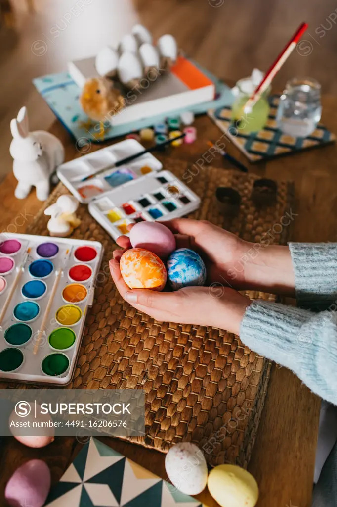 From above cropped anonymous person demonstrating finished Easter egg over table with watercolor at home