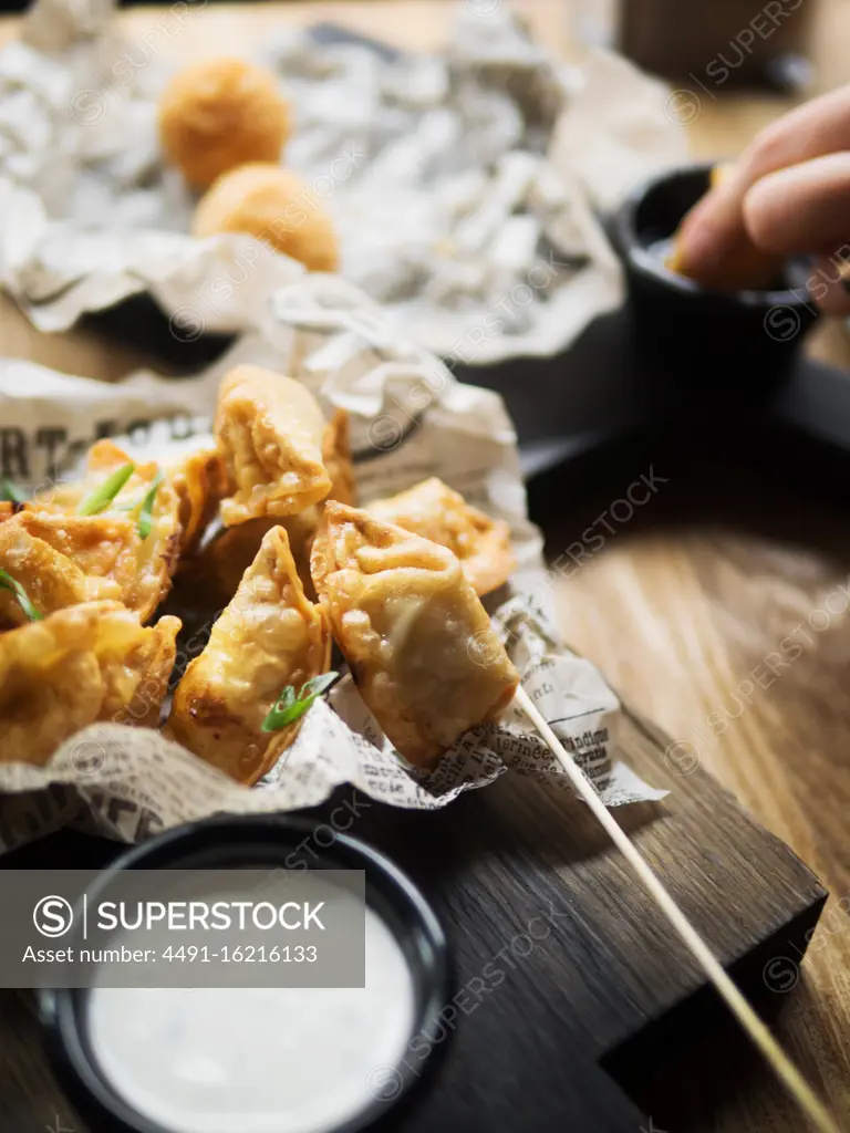 Delicious deep fried dumplings garnished with green herbs placed on paper served with white sauce on wooden table