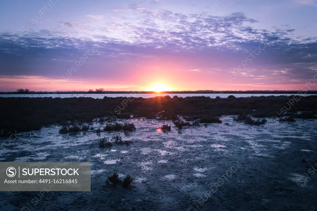 Amazing tranquil scenery of colorful sundown sky with clouds over calm dark wetlands