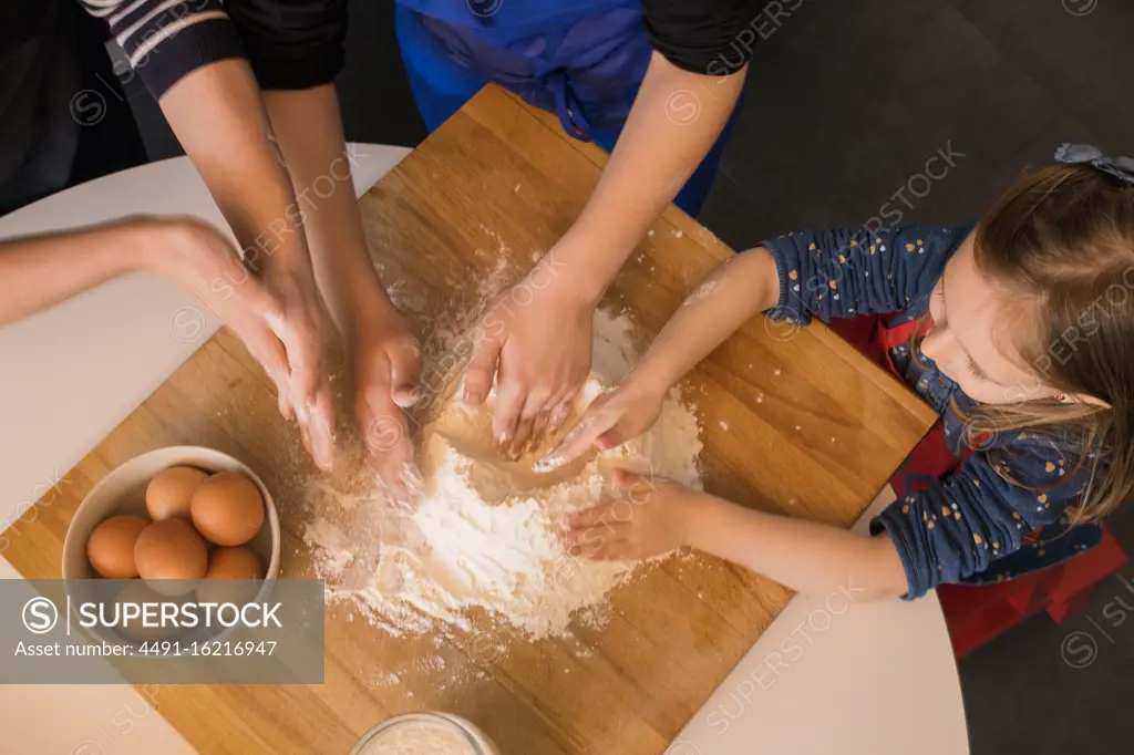 Children preparing dough while standing together at kitchen table with flour