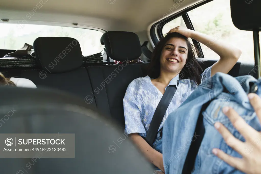 Young laughing woman posing on backseat of car holding eyes closed.