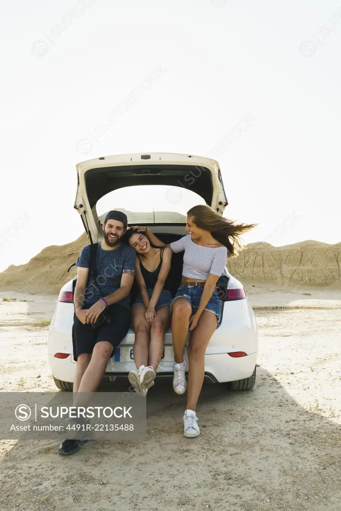 Cheerful man and women friends sitting in car trunk and having fun together.