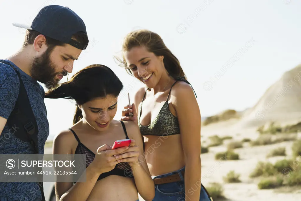 Cheerful young women and man standing in nature together and browsing smartphone.