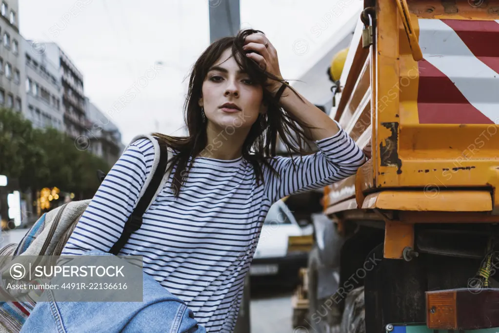 Pretty sensual tourist woman looking at camera while leaning on truck on city street.