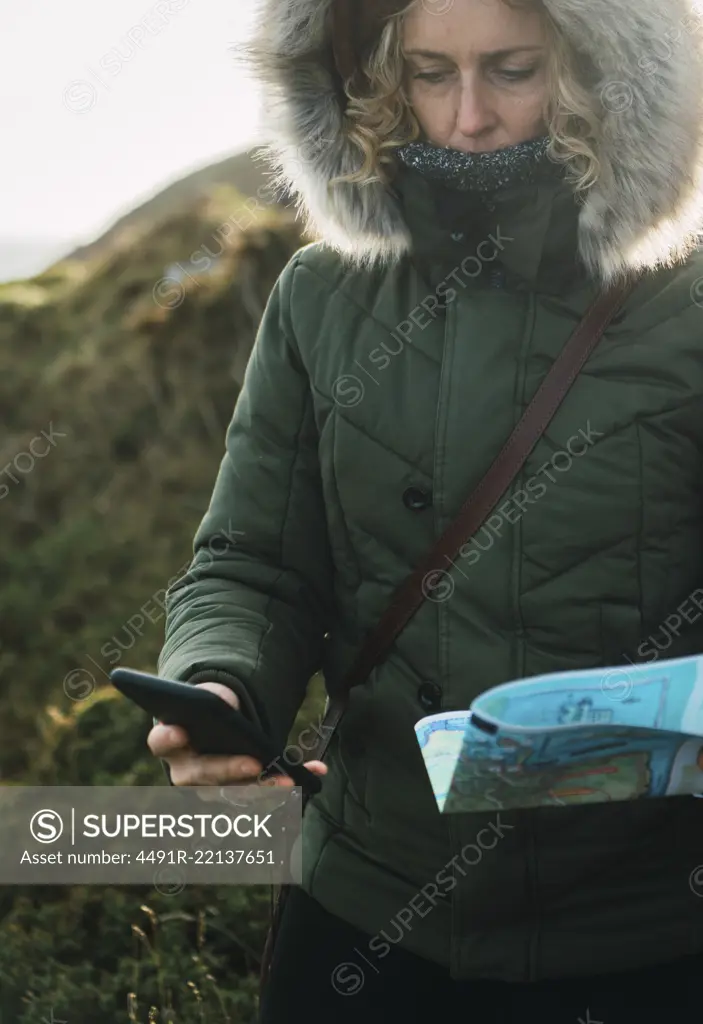 Pretty woman tourist with smartphone and map navigating in mountains.