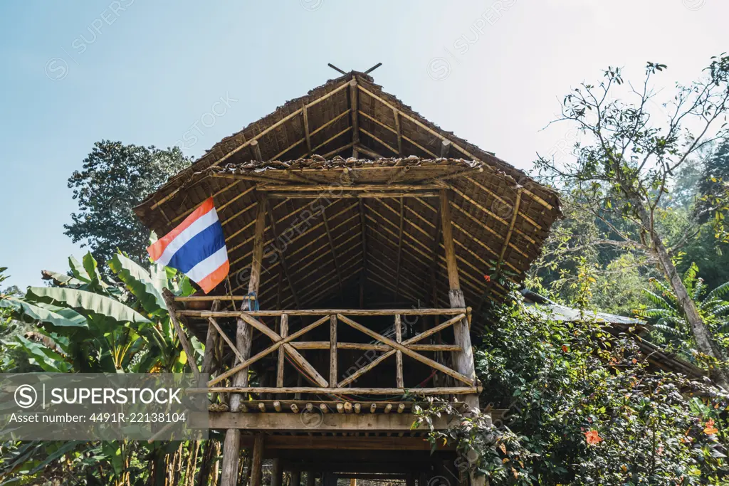 From below view to small wooden house with flag placed in green nature in sunny day.