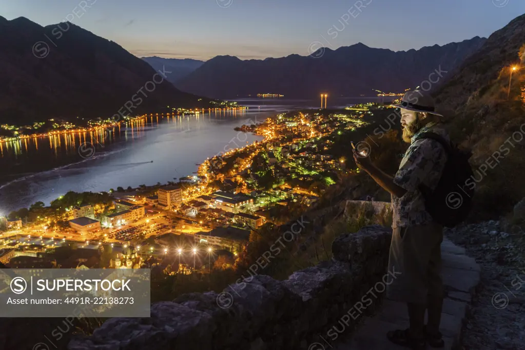 Tourist man using smartphone on mountain at town with illumination at night.