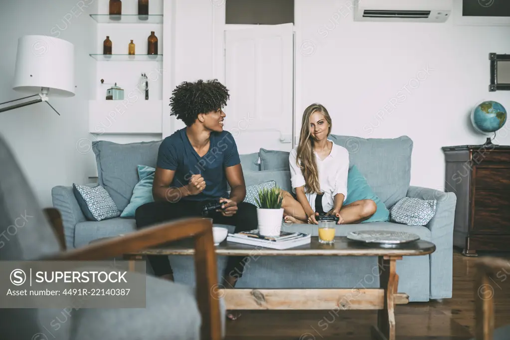 Happy young interracial couple relaxed at home on the sofa having fun playing video games 