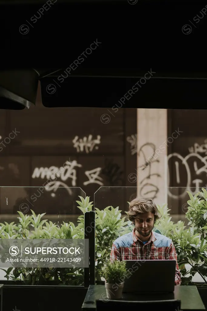 Young bearded man in outdoor cafe working on laptop