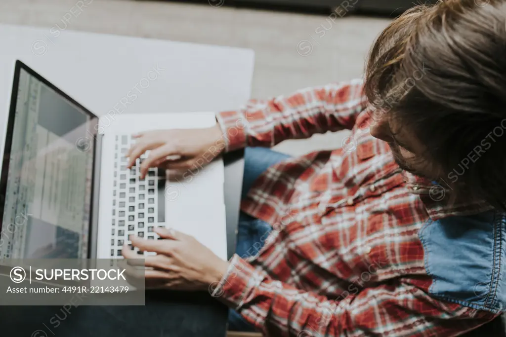 Close-up of brunet man in casual shirt typing on laptop in outdoor cafe in daylight.From above