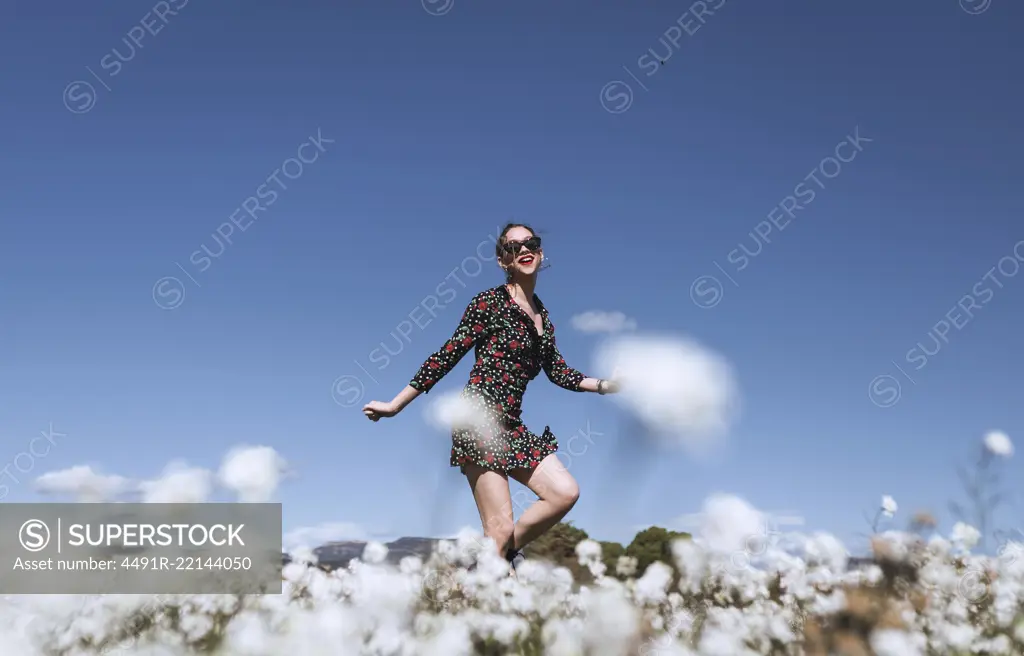 Attractive young woman in sunglasses standing on white field with flowers.