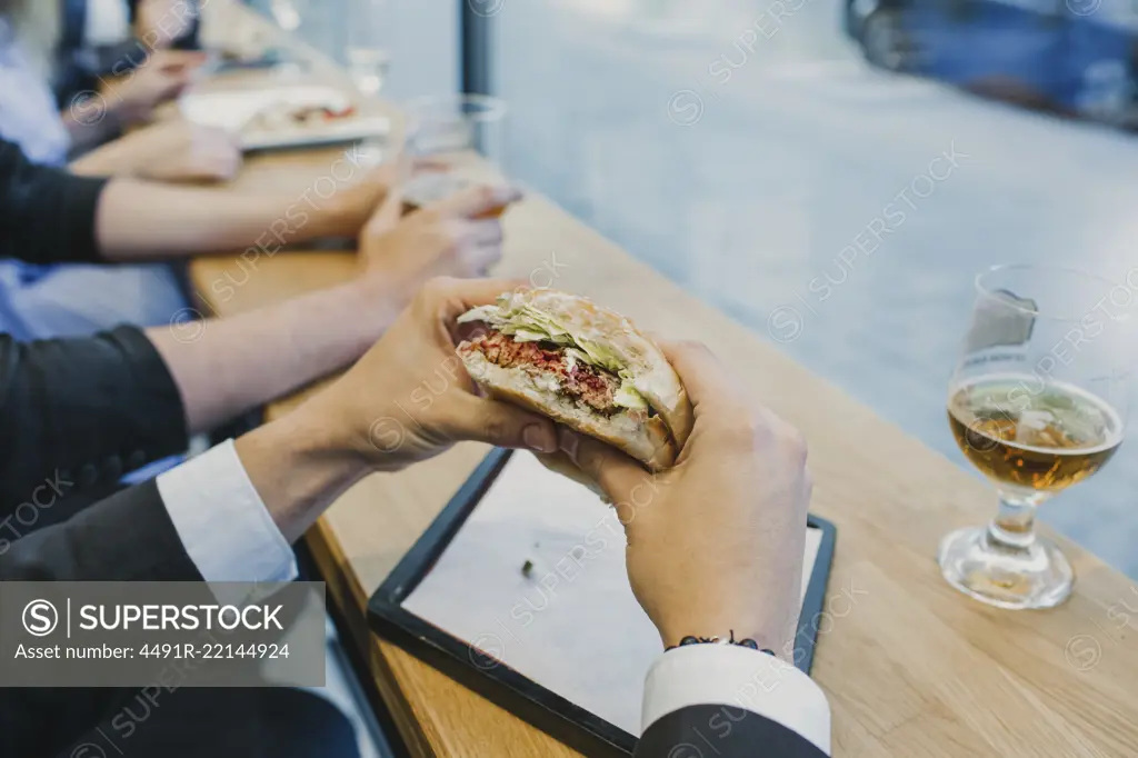 Hand of unrecognizable man in suit holding tasty burger in cafe.