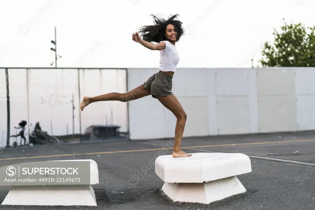 Happy black woman jumping on concrete blocks and looking at camera.