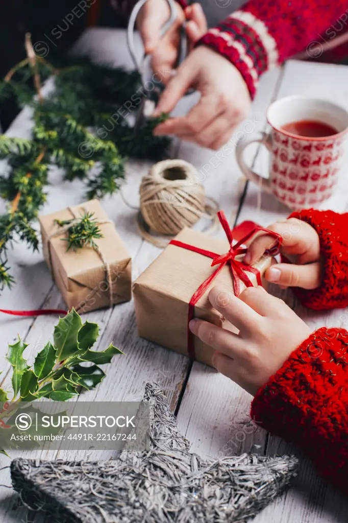 Kid and woman wrapping presents for Christmas on a wooden table with handcraft decoration 