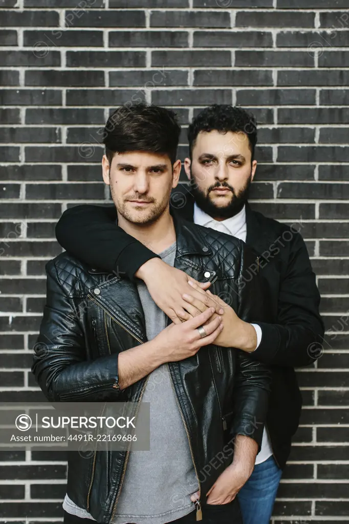 Gay couple hugging near brick wall