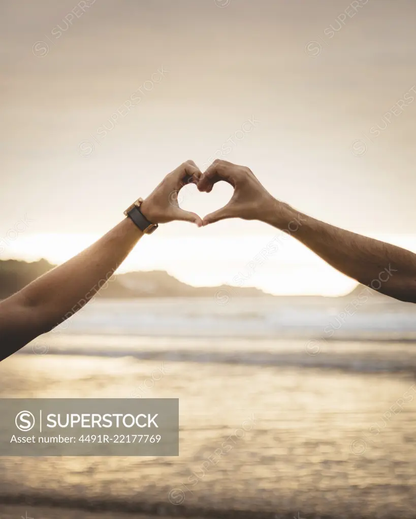 Two unrecognizable men gesturing heart with hands in sunset lights. 