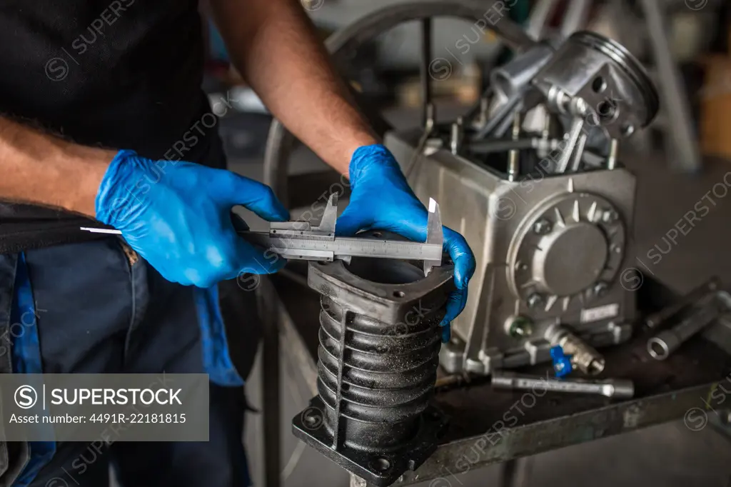 Close-up of a mechanic using a vernier caliper to measure a cylinder from a compressor engine