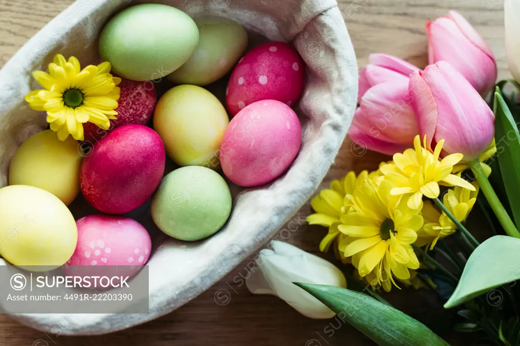 Closeup bunch of fresh flowers and basket with colored eggs placed on lumber tabletop