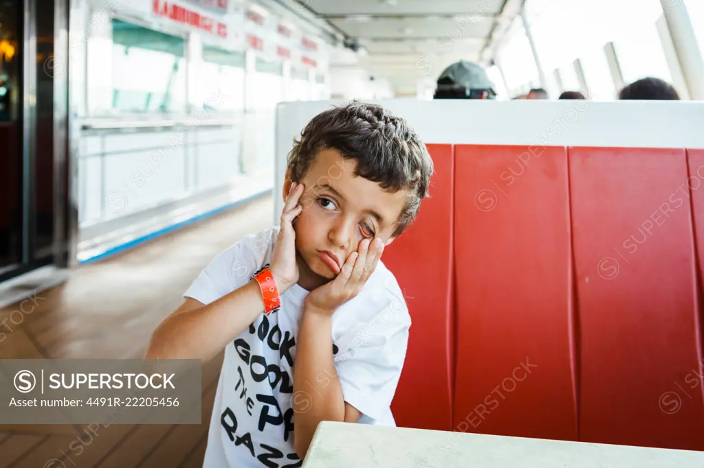 Funny kid making face with hands on face and sitting at table