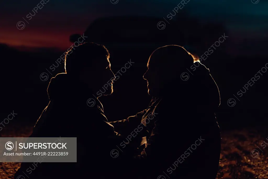 Side view of homosexual couple embracing and sitting on meadow in evening