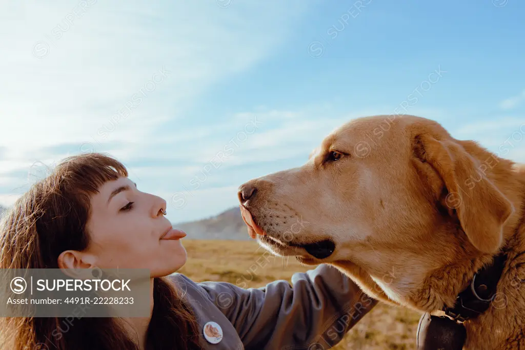 Side view of young hipster stroking funny dog between meadow and blue sky