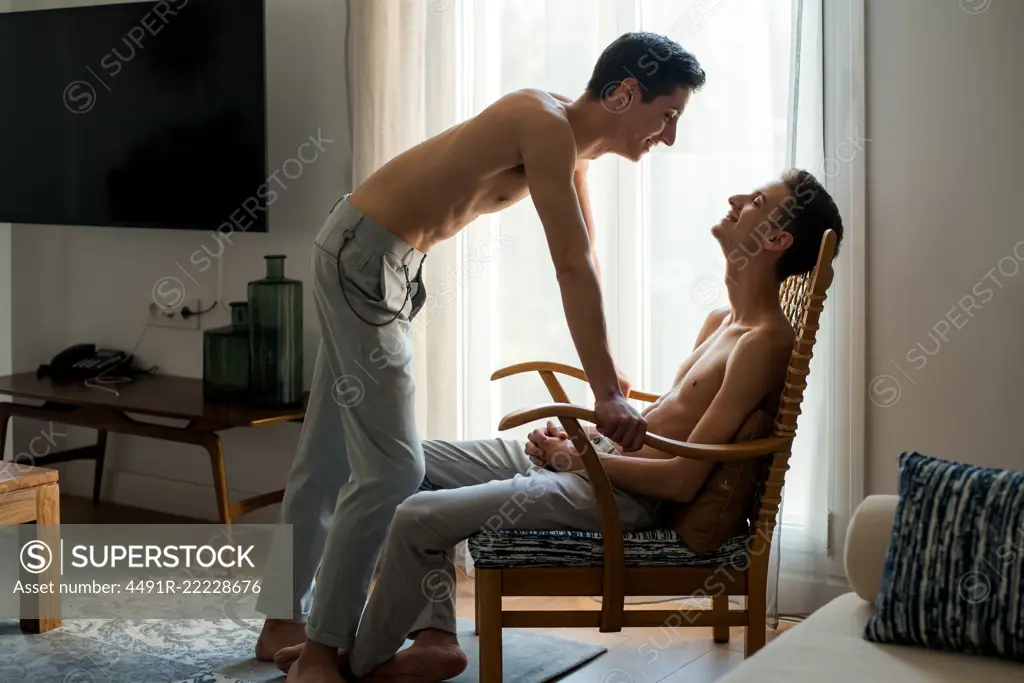 Stylish shirtless gay couple posing while sitting in a chair