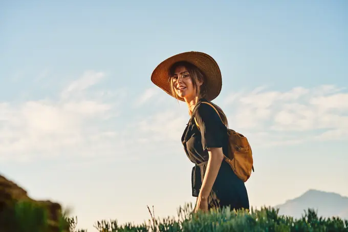 Side view of female tourist wearing a straw hat and backpack walking