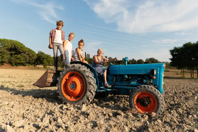 Elderly woman driving tractor while working on agriculture field on sunny day on farm