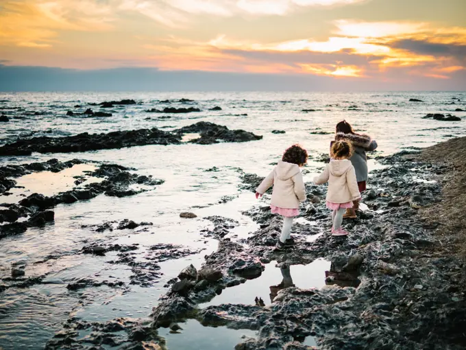 anonymous little girls from behind standing by the beach on rocks looking at the sea on a winter day