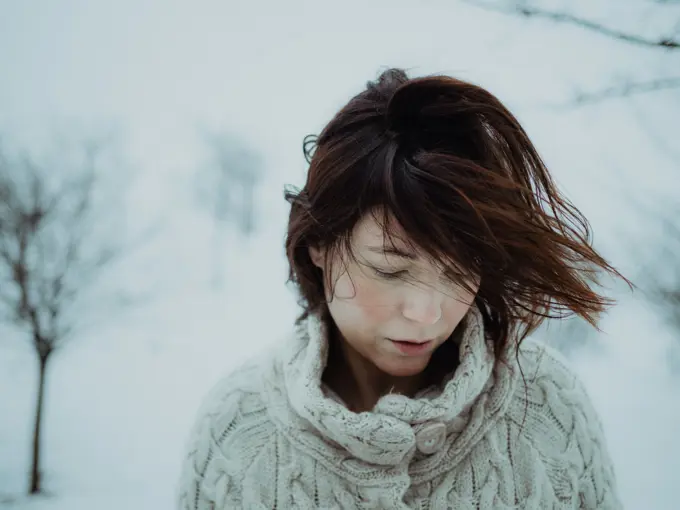 Portrait of pensive attractive brunette in white sweater on background of snowy area