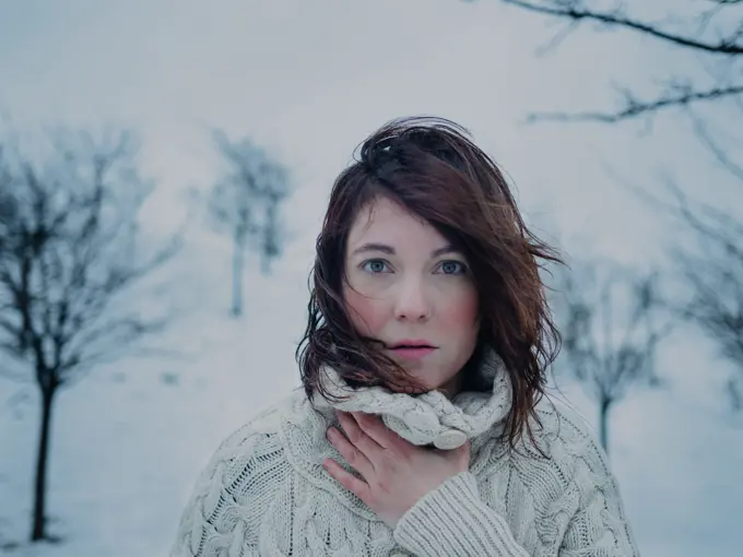 Portrait of pensive attractive brunette in white sweater on background of snowy area