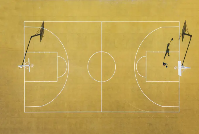 Young man playing basketball on outdoor court. Top view, bird eye view of yellow basketball court