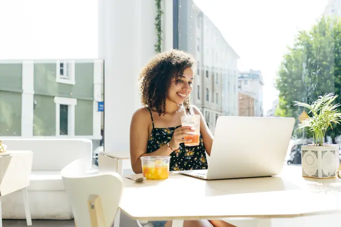 Ethnic female with laptop enjoying healthy drink in cafe