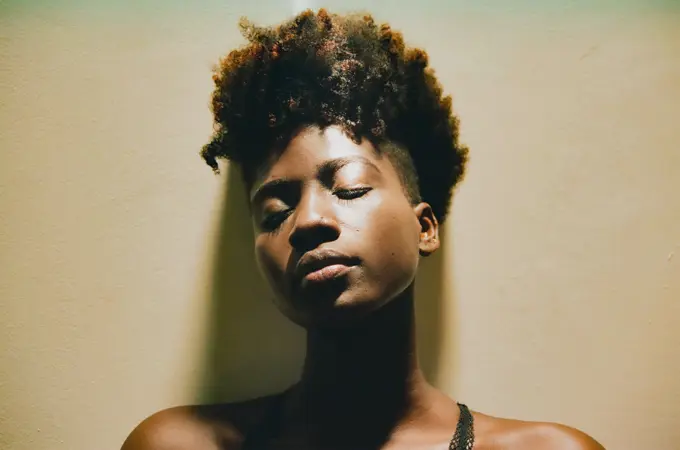 African American with afro hair sensual with closed eyes and natural makeup leaning on wall