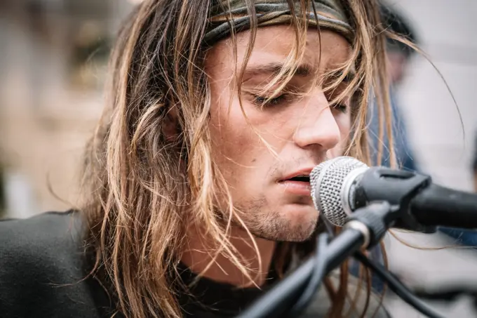 Close-up portrait of expressive street singer man with long hair singing in the street