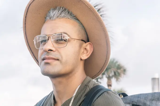 Young man expressing joy and posing for a photo in glasses and a brown hat. Portrait