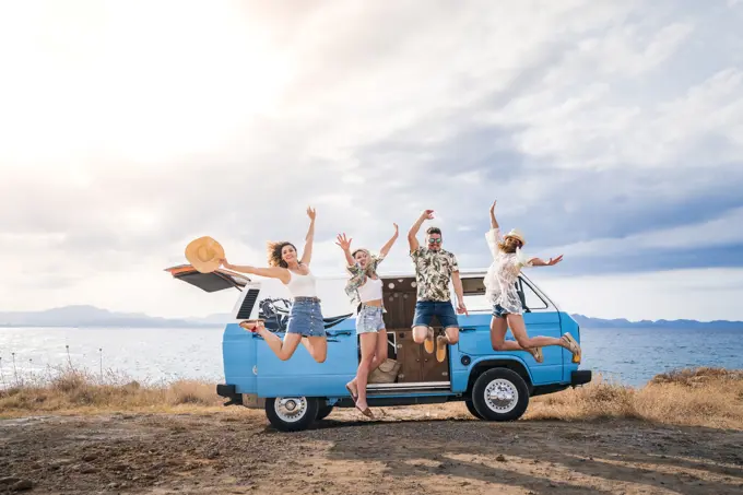 Cheerful tourist jumping raising hands and legs on background of bright minivan on beach in sunny day