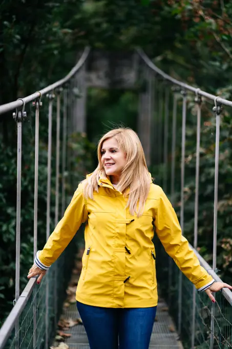 Cheerful female tourist standing on hanging bridge in summer