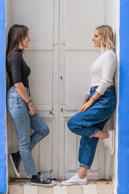 Side view of happy gentle caring girlfriends in stylish outfit standing near door looking at each other