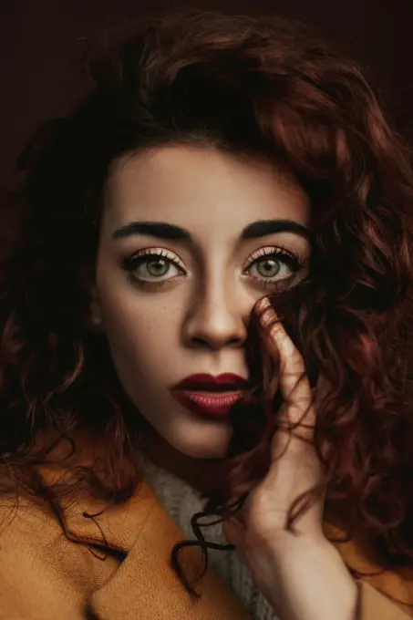 Young curly brown haired female in casual holding strand of hair in hand next to face while looking at camera with big grey eyes;Curly haired woman with big grey eyes in casual