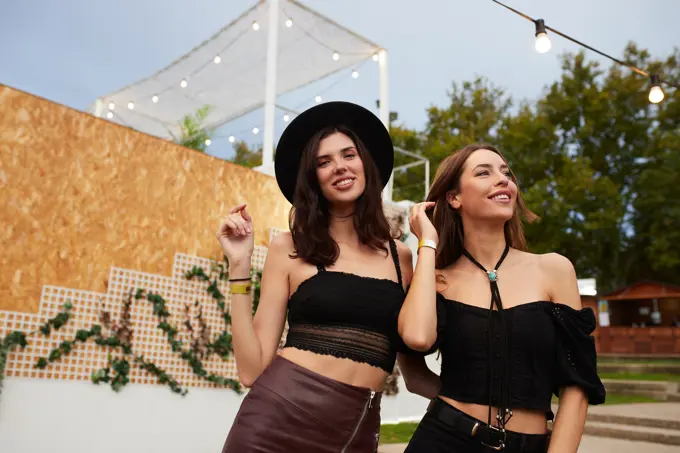 Charming long haired stylish girl friends having fun in bright day at festival