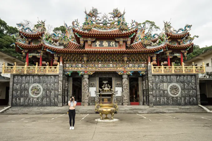 Female traveler in casual wear taking picture in front of camera with beautiful Taoist Temple Dai Quan Tang at Taiwan;Female tourist with photo camera visiting aged oriental temple